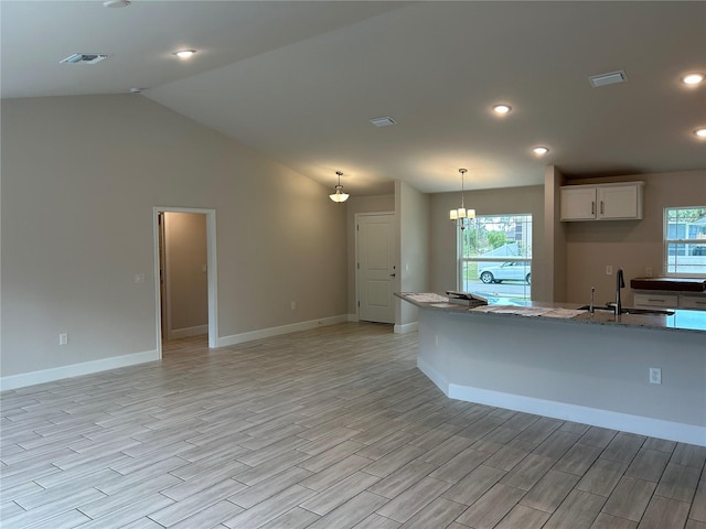 kitchen featuring a wealth of natural light, decorative light fixtures, sink, white cabinets, and light stone counters