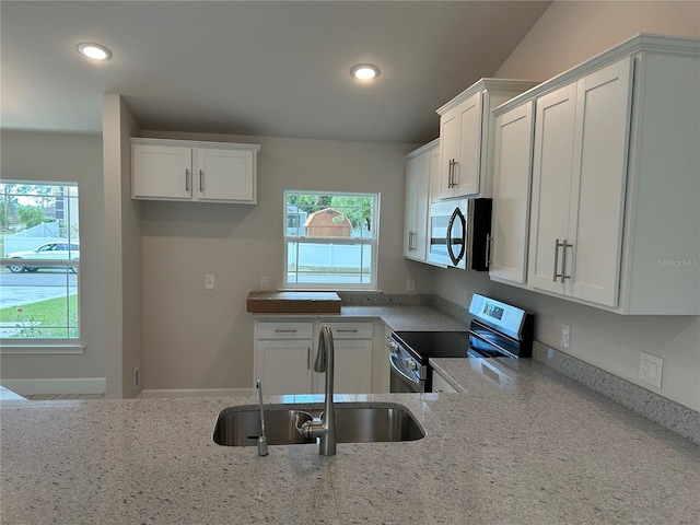 kitchen featuring appliances with stainless steel finishes, plenty of natural light, white cabinetry, sink, and light stone countertops