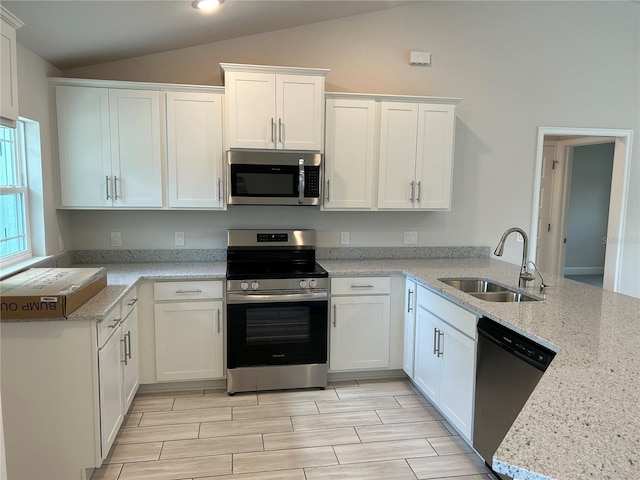 kitchen featuring stainless steel appliances, vaulted ceiling, sink, and white cabinets