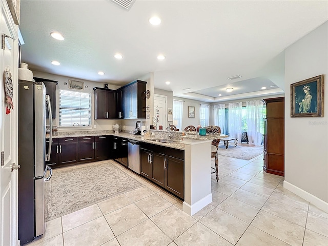 kitchen with a tray ceiling, light stone counters, kitchen peninsula, and a healthy amount of sunlight