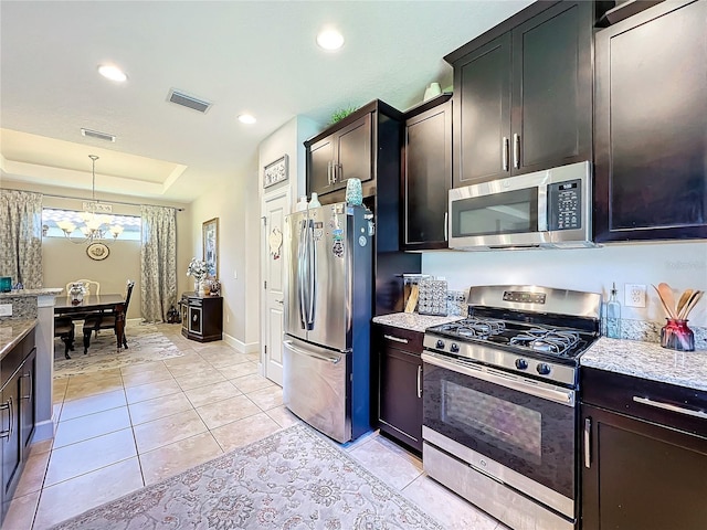 kitchen featuring an inviting chandelier, decorative light fixtures, light stone countertops, appliances with stainless steel finishes, and a tray ceiling