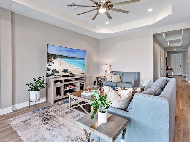 living room featuring ceiling fan, a tray ceiling, and light hardwood / wood-style floors