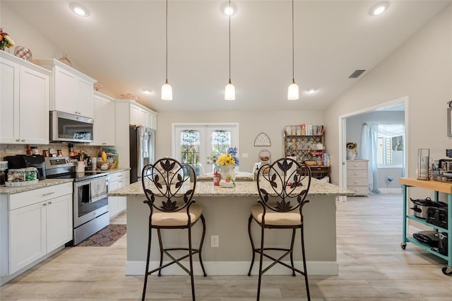 kitchen with a center island with sink, white cabinetry, stainless steel appliances, and a kitchen bar