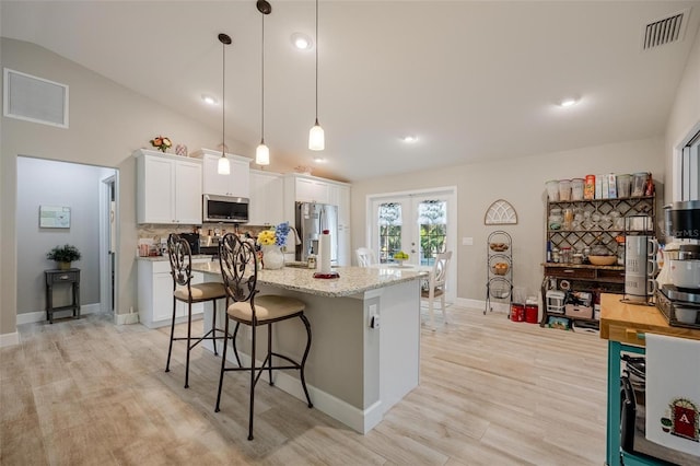 kitchen with vaulted ceiling, french doors, appliances with stainless steel finishes, white cabinets, and light hardwood / wood-style floors