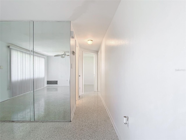 hallway with visible vents, baseboards, and speckled floor