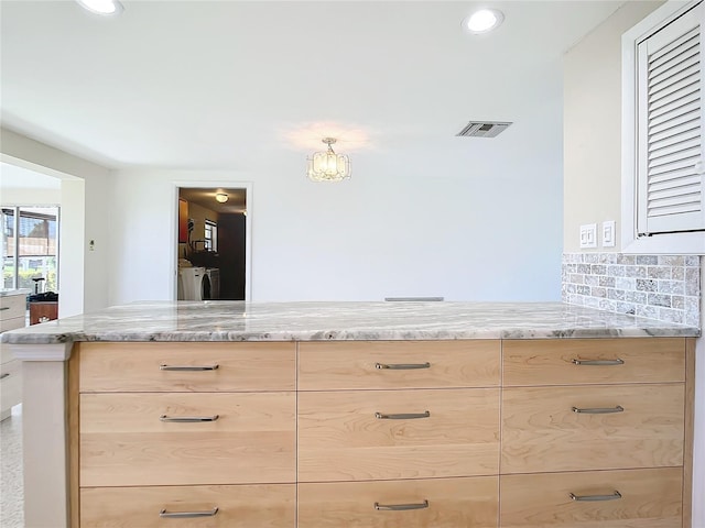 kitchen featuring light brown cabinetry, independent washer and dryer, backsplash, and light stone countertops