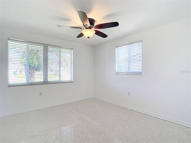 empty room featuring ceiling fan, baseboards, and speckled floor