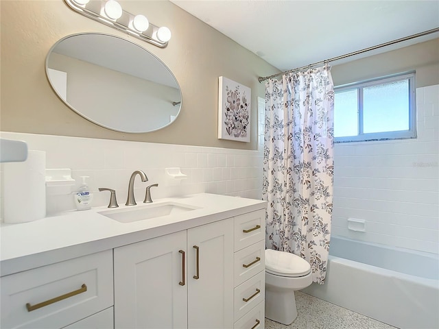 full bathroom featuring toilet, speckled floor, shower / bath combo with shower curtain, vanity, and tile walls