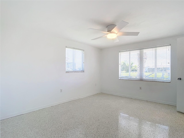 empty room featuring ceiling fan, plenty of natural light, baseboards, and speckled floor