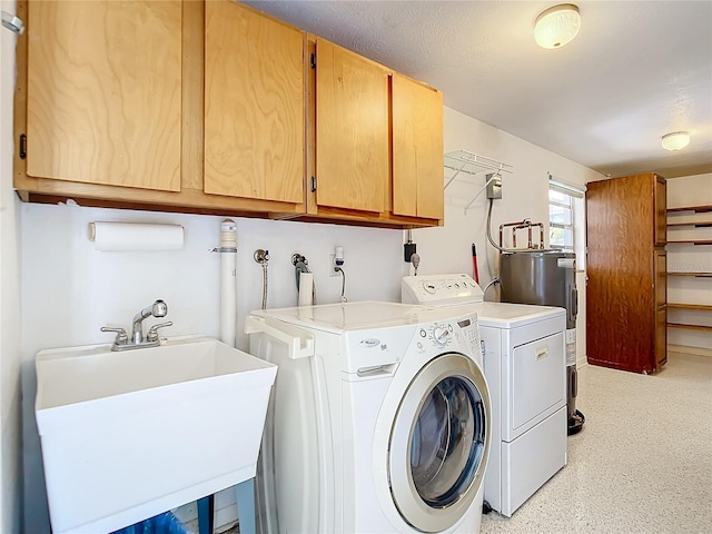 clothes washing area with electric water heater, cabinets, sink, and washing machine and dryer