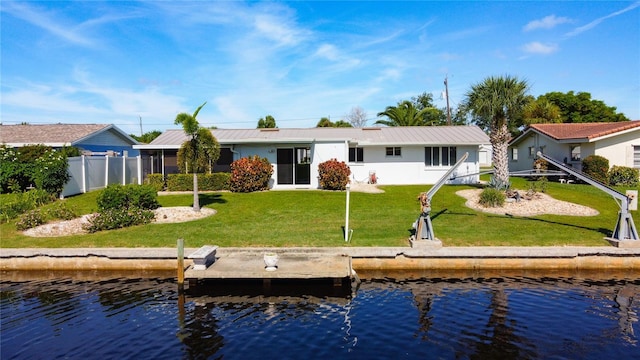 back of house featuring metal roof, a lawn, a water view, and fence