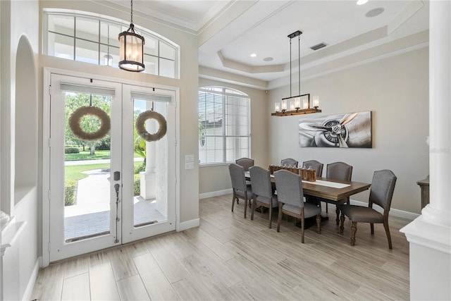 dining area with a raised ceiling, light wood-type flooring, ornamental molding, and french doors