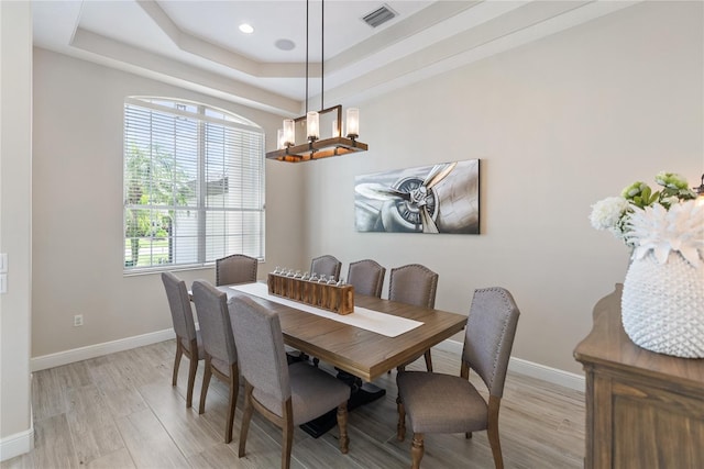 dining space with a tray ceiling and light hardwood / wood-style flooring