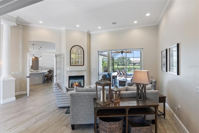 living room with decorative columns, crown molding, sink, and light hardwood / wood-style floors