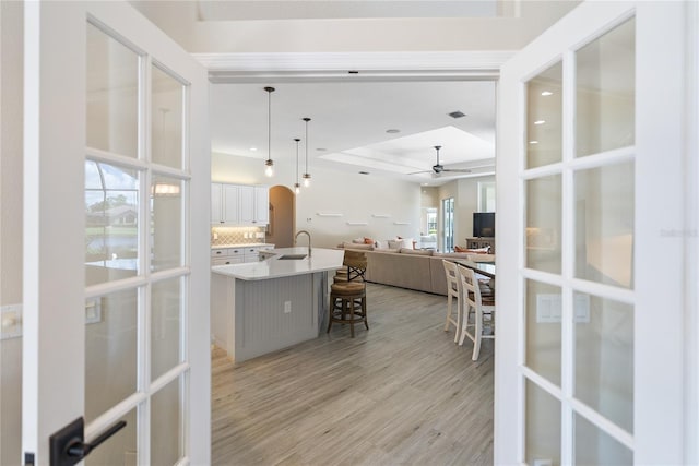 kitchen with white cabinets, hanging light fixtures, ceiling fan, light hardwood / wood-style floors, and a breakfast bar area