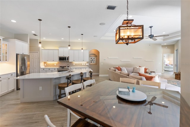 dining space with light wood-type flooring, a raised ceiling, ceiling fan, and sink