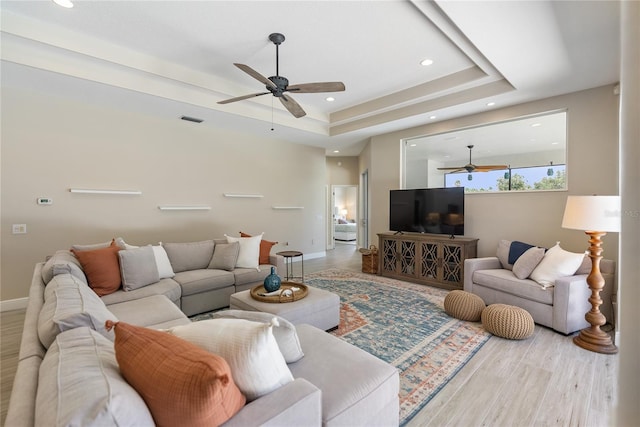 living room featuring hardwood / wood-style flooring, ceiling fan, and a raised ceiling