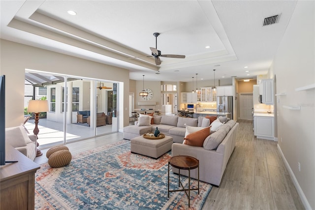 living room featuring a tray ceiling, ceiling fan with notable chandelier, and light wood-type flooring