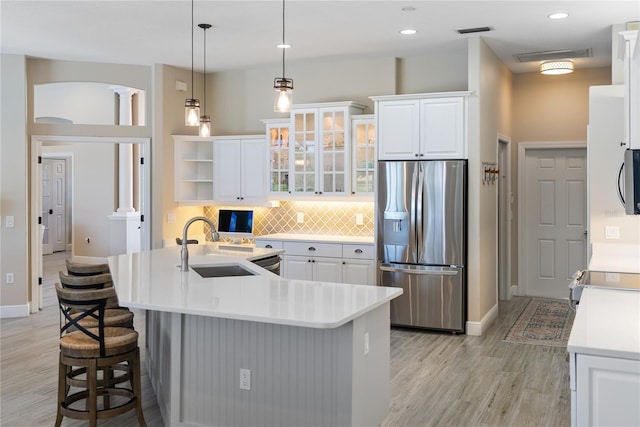 kitchen featuring light wood-type flooring, stainless steel appliances, sink, pendant lighting, and white cabinetry