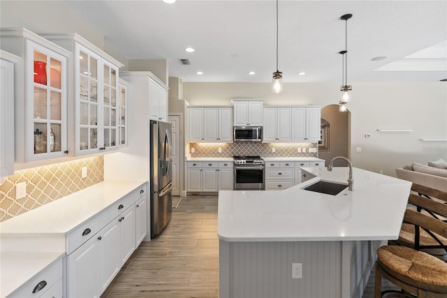 kitchen featuring white cabinetry, sink, hanging light fixtures, stainless steel appliances, and light wood-type flooring