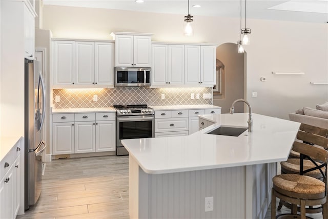 kitchen featuring appliances with stainless steel finishes, light wood-type flooring, sink, white cabinetry, and hanging light fixtures