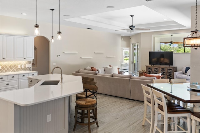 kitchen with a center island with sink, white cabinetry, a tray ceiling, and sink