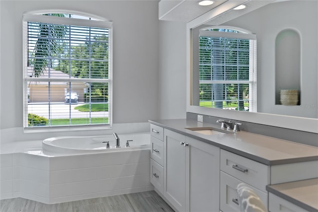 bathroom with vanity, a relaxing tiled tub, and a wealth of natural light