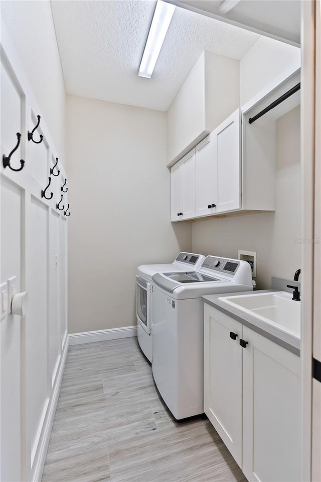 laundry room with cabinets, sink, washer and dryer, light wood-type flooring, and a textured ceiling