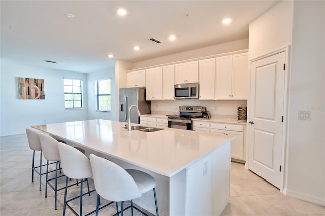 kitchen with appliances with stainless steel finishes, an island with sink, a breakfast bar, sink, and white cabinetry