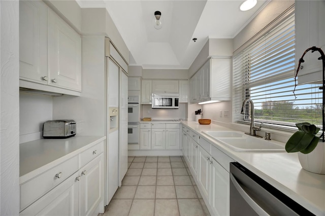 kitchen with a raised ceiling, white cabinetry, light tile patterned flooring, sink, and white appliances