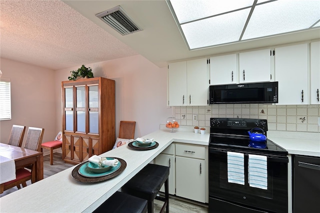 kitchen featuring a healthy amount of sunlight, backsplash, light hardwood / wood-style floors, white cabinets, and black appliances