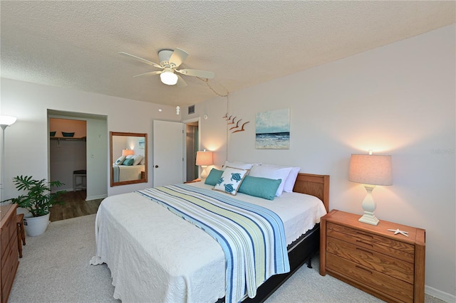 carpeted bedroom featuring a textured ceiling, a walk in closet, a closet, and ceiling fan