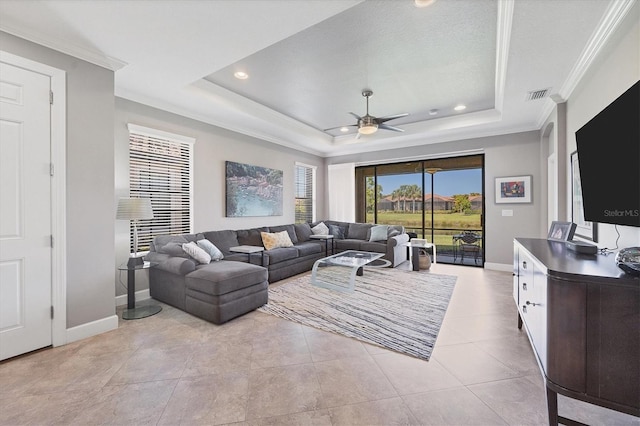 living room with a tray ceiling, light tile patterned floors, crown molding, and ceiling fan