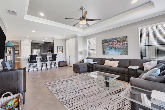 living room with light tile patterned floors, a tray ceiling, ceiling fan, and ornamental molding