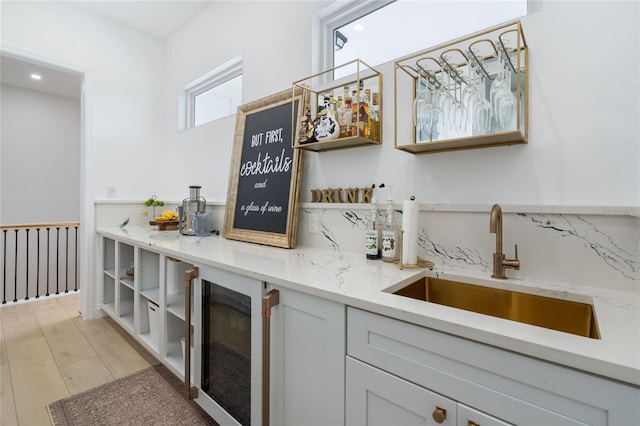 bar featuring sink, decorative backsplash, light stone countertops, light wood-type flooring, and beverage cooler