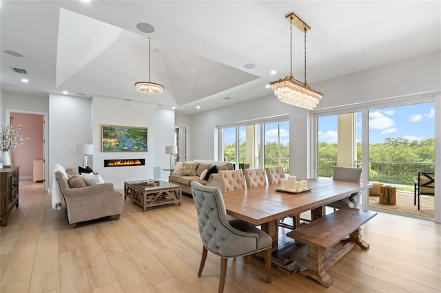 dining area with light wood-type flooring, a raised ceiling, and a notable chandelier