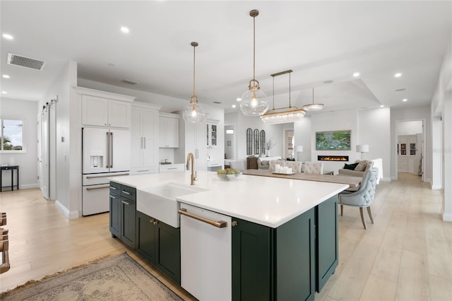 kitchen with sink, pendant lighting, white appliances, a kitchen island with sink, and white cabinets