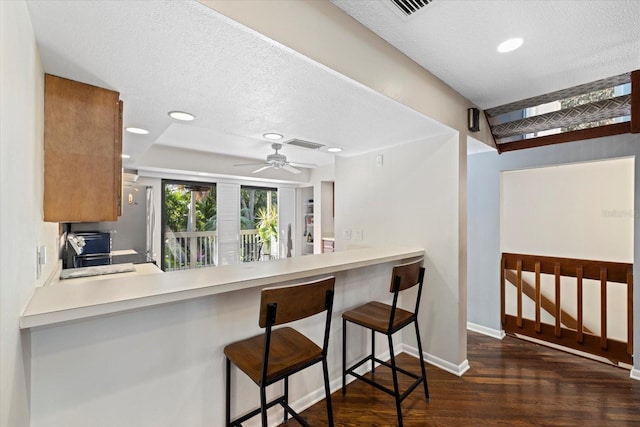 kitchen with a kitchen breakfast bar, a textured ceiling, ceiling fan, and dark wood-type flooring