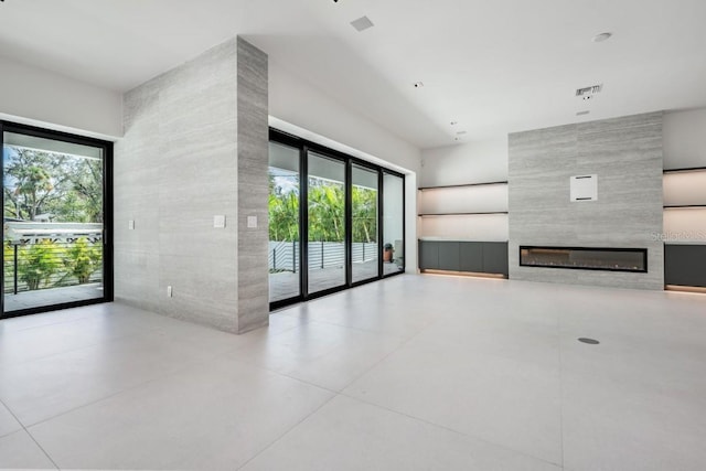 unfurnished living room featuring a healthy amount of sunlight, a large fireplace, tile walls, and light tile patterned floors