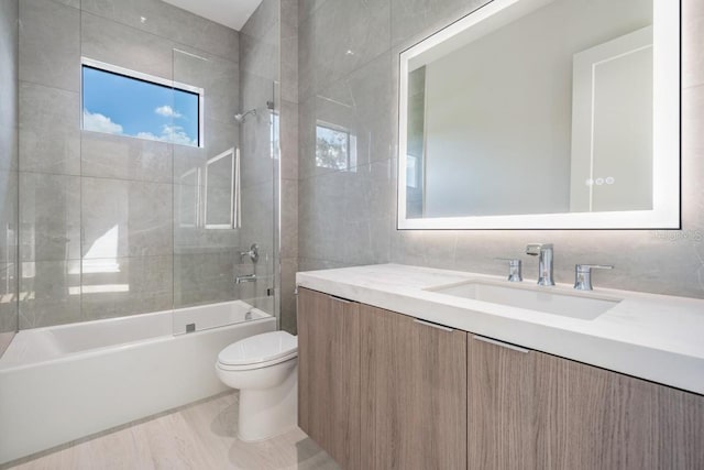 full bathroom with hardwood / wood-style flooring, toilet, vanity, tiled shower / bath combo, and tile walls