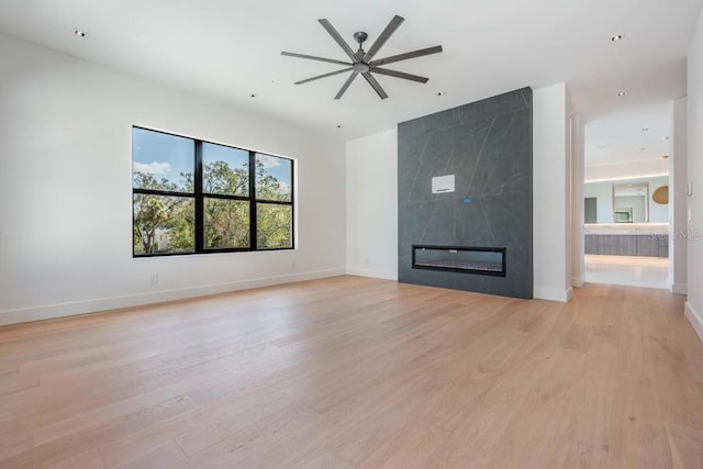 unfurnished living room with light hardwood / wood-style flooring, a large fireplace, and ceiling fan