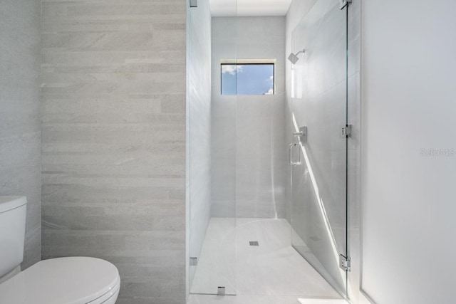 bathroom featuring toilet, tile walls, and a shower with door