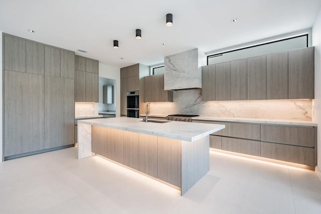 kitchen featuring decorative backsplash, stainless steel appliances, a center island with sink, sink, and light brown cabinetry