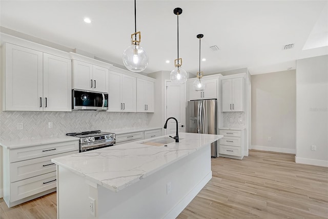 kitchen with a sink, visible vents, white cabinets, appliances with stainless steel finishes, and a center island with sink