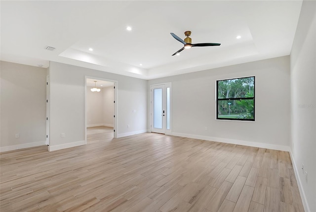 empty room featuring a tray ceiling, recessed lighting, light wood-style flooring, ceiling fan, and baseboards