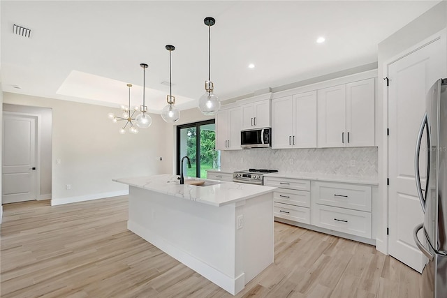 kitchen featuring a center island with sink, decorative backsplash, light stone counters, appliances with stainless steel finishes, and a sink