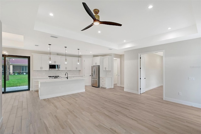 kitchen featuring a tray ceiling, tasteful backsplash, light countertops, appliances with stainless steel finishes, and light wood-style floors