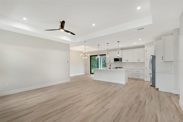 kitchen featuring open floor plan, appliances with stainless steel finishes, light wood-type flooring, decorative backsplash, and a tray ceiling