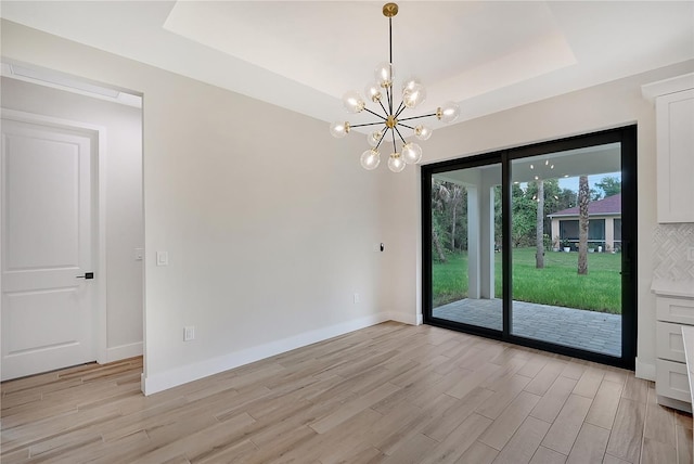 spare room with baseboards, an inviting chandelier, a raised ceiling, and light wood-style floors