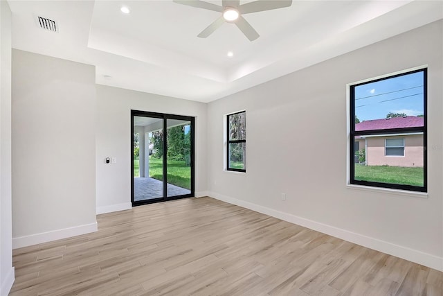 empty room with a tray ceiling, baseboards, light wood finished floors, and recessed lighting